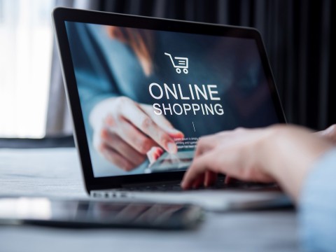 Online-Shopping mit Smartphone-App und Kreditkarte. Laptop mit geöffneter Online-Shopping-Website, Hand zeigt auf den Bildschirm.