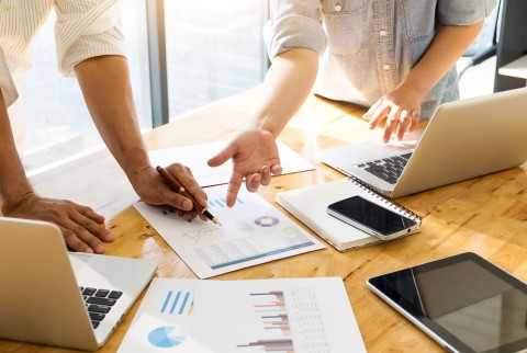 Menschen arbeiten gemeinsam an einem Tisch mit Laptops, Dokumenten und Diagrammen, Symbol für Teamarbeit und Datenanalyse.