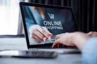 Laptop mit geöffneter Online-Shopping-Website, Hände halten eine Kreditkarte vor dem Bildschirm.