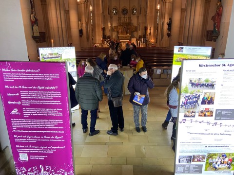 Zahlreiche Interessierte stehen vor leuchtenden Displays in der stimmungsvoll beleuchteten Kirche St. Agatha.
