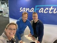 Annika Kilch, Oliver Unland und ein Mitarbeiter von SanaFactur am Messestand mit blauem Branding