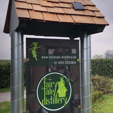 Grünes Schild mit Aufschrift „fairytale distillery“ und Kontaktdaten im Fokus