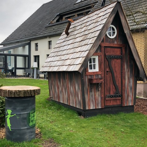 Schräg gebautes Verkaufshäuschen aus Holz mit Schindeldach vor dem Gebäude der Fairytale Distillery