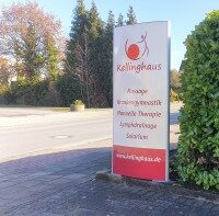 Außenaufnahme eines Aluminium-Pylons mit rotem Text auf reflektierender weißer Folie. Die Werbestele steht am Straßenrand und bewirbt ein Therapiezentrum.