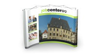 Messestand des Jobcenters Osnabrück mit großem Stadtbild und Servicefotos. Gebogener Messestand mit großem Bild des historischen Osnabrücker Rathauses und kleineren Fotos zur Jobvermittlung, Branche Dienstleistung.