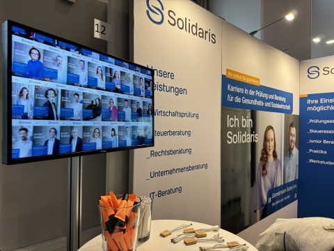 Moderner Messeauftritt von Solidaris mit Video-Screen und Give-aways für junge Talente Solidaris Messestand mit Monitorwand, Broschüren und Werbemitteln zur Mitarbeitergewinnung