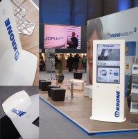 Moderner Messestand mit weißen Designdisplays und digitaler Präsentationsstele der Firma Krone, umgeben von Sitzmöbeln und Messebesuchern.