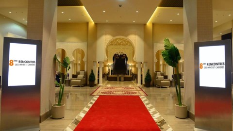 Zwei digitale Designstelen links und rechts eines roten Teppichs im eleganten Hoteleingang, zeigen Veranstaltungsinformationen in modernem Ambiente.