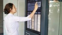 Frau bedient interaktive digitale Stele mit großem Touchdisplay, um Informationen aus einer digitalen Bibliothek abzurufen.