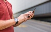 Mann in rotem T-Shirt nutzt Smartphone zur Zeiterfassung im urbanen Umfeld.