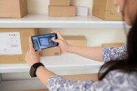 Smartphone-App zur Bestandsaufnahme und Dokumentation im Malerbetrieb, Frau fotografiert Kartons im Lager.