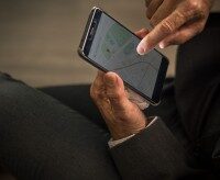 Person in Anzug nutzt Smartphone-App zur Standortbestimmung mit Karte, Einsatz im Garten- und Landschaftsbau zur digitalen Einsatzplanung.