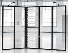 Faltbare Präsentationswand mit Glasoptik – mobile Messewand für moderne Ausstellungen Schwarze faltbare Präsentationswand mit transparenten Flächen in einem lichtdurchfluteten Raum