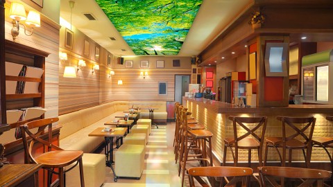 Leuchtbild an der Decke – stimmungsvolle Raumgestaltung für Gastronomie und Innenräume Großes Deckenleuchtbild mit Naturmotiv in einem Café mit Holzmöbeln