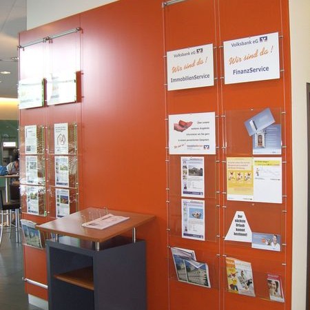 Rote Wand mit transparenten Prospekthaltern und Informationsflyern, Beispiel für funktionale Innenbeschilderung in einer Bankfiliale