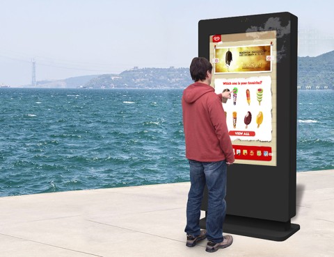 Ein Mann steht vor einem freistehenden Multi-Touch-Bildschirm am Wasser und wählt ein Eis auf dem Bildschirm aus.