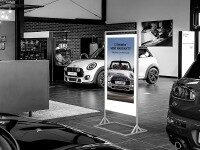 Freistehendes Digital Signage Display mit MINI-Werbung in einem Autohaus, im Hintergrund mehrere ausgestellte Fahrzeuge