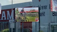 Eingang eines Baufachzentrums mit Werbeschildern und Fahrradangeboten