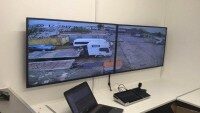 Kontrollraum mit Überwachungssystemen Kontrollraum mit zwei großen Monitoren, die Überwachungsaufnahmen eines Parkplatzes zeigen, Laptop daneben
