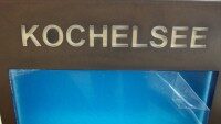 Logo Kochelsee Logo mit dem Schriftzug Kochelsee auf einem bronzenen Schild