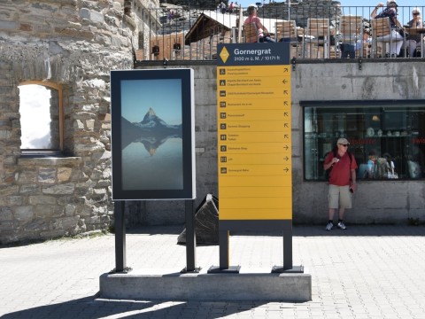 Outdoor-Digital Signage Stele mit Display am Gornergrat neben Wegweiser, Hintergrund Matterhorn-Gebiet
