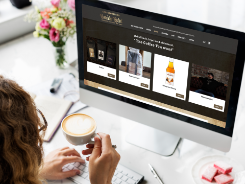 Frau trinkt Kaffee und betrachtet die Website Barista Rebel mit Produktangeboten am Computer