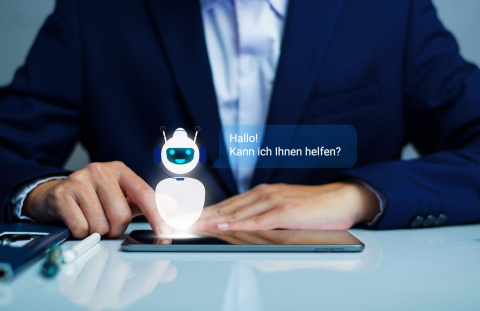 Geschäftsmann interagiert mit einem digitalen Assistenten auf einem Tablet, Sprechblase mit 'Hallo! Kann ich Ihnen helfen?'