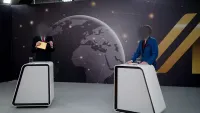 TV Studio mit BIGUP-Kollektion als Rückwand und zwei Moderatoren an Stehpulten