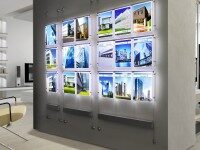 Flyshine Schaufensterwerbung mit mehreren Immobilien-Exposés an einer Wand, Beispiel für hochwertige Innenbeschilderung und Präsentationssysteme