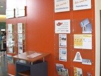 Rote Wand mit transparenten Prospekthaltern und Informationsflyern, Beispiel für funktionale Innenbeschilderung in einer Bankfiliale
